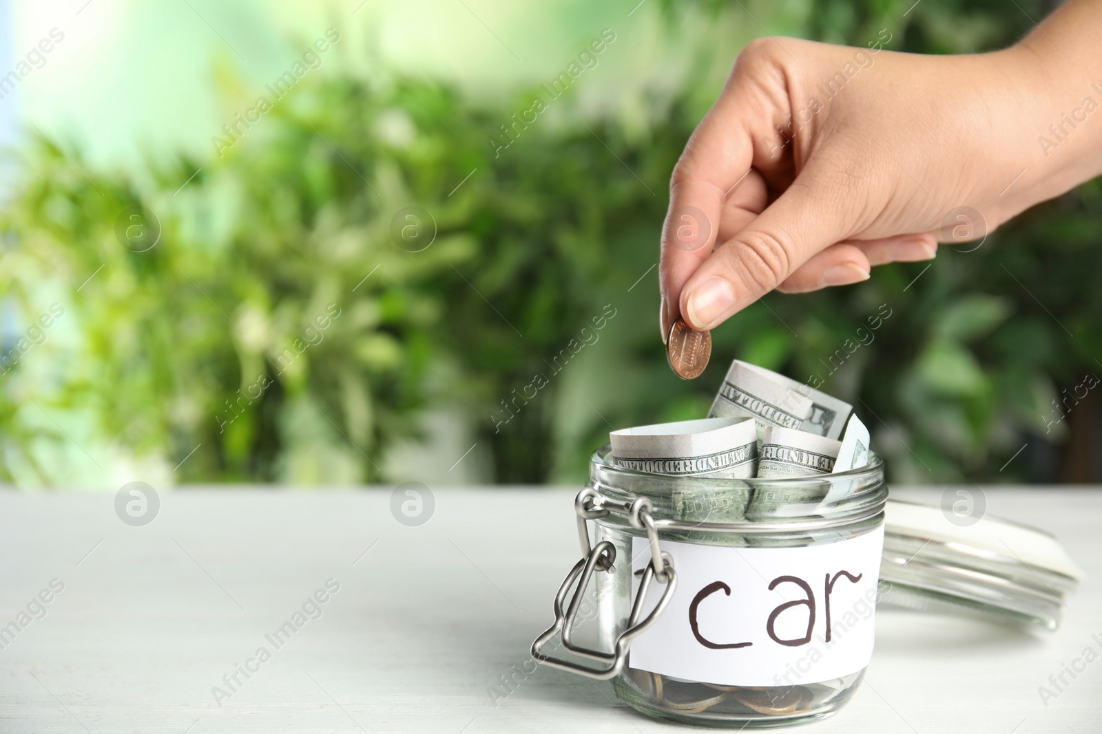 Photo of Woman putting coin into jar with tag CAR on white wooden table, closeup. Space for text