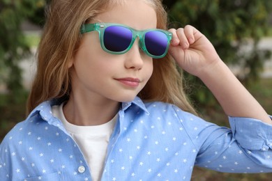 Photo of Girl in stylish sunglasses near spruce trees outdoors, closeup