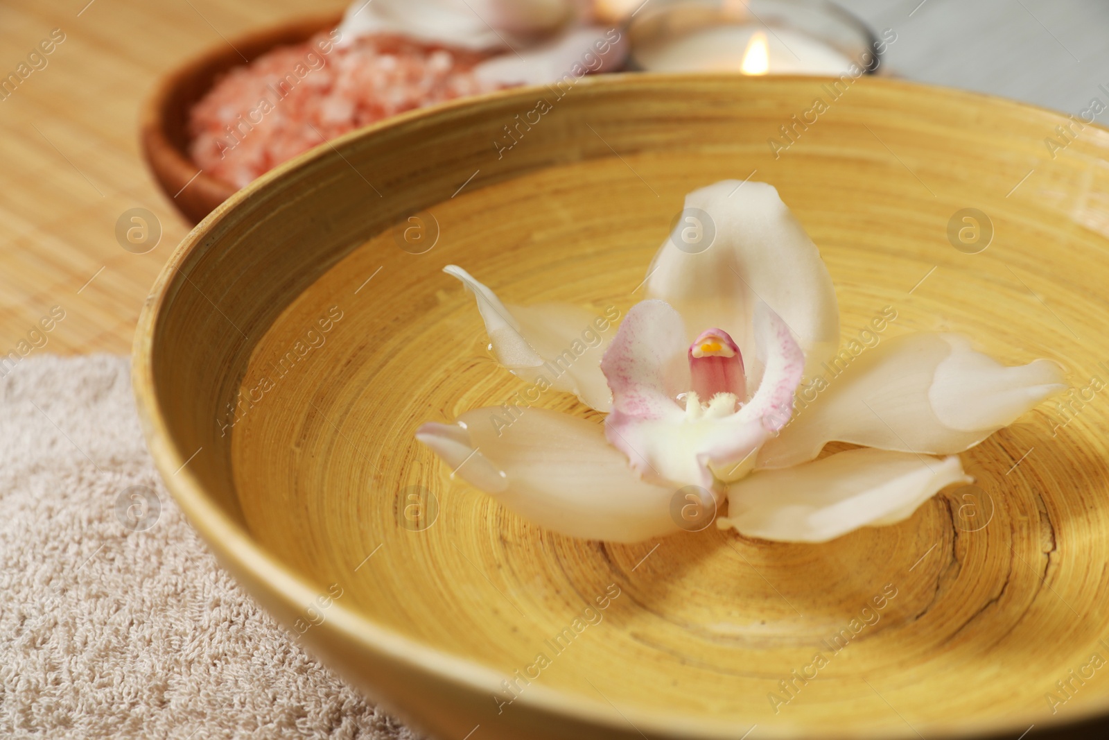 Photo of Bowl with water and beautiful flower on bamboo mat, closeup. Spa treatment