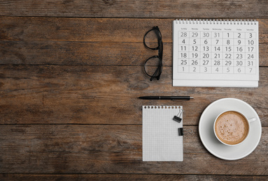 Flat lay composition with calendar and cup of coffee on wooden table. Space for text