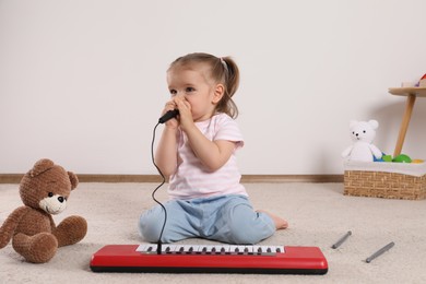Photo of Cute little girl singing with toy piano and microphone at home