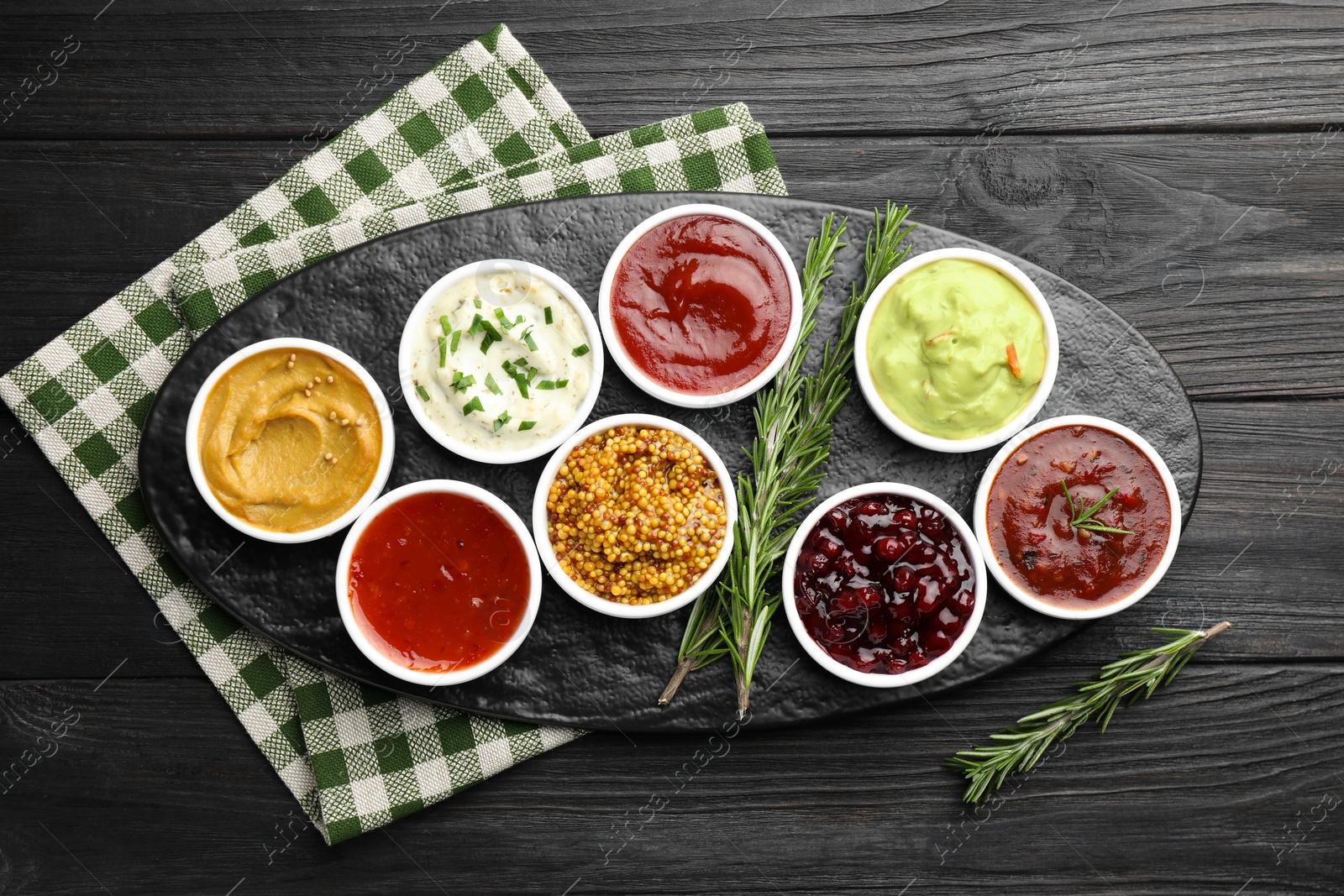 Photo of Different tasty sauces in bowls and rosemary on black wooden table, top view