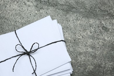 Photo of Stack of letters tied with string on grey table, top view. Space for text