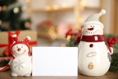 Christmas composition with decorative snowmen near white blank card on table, space for text