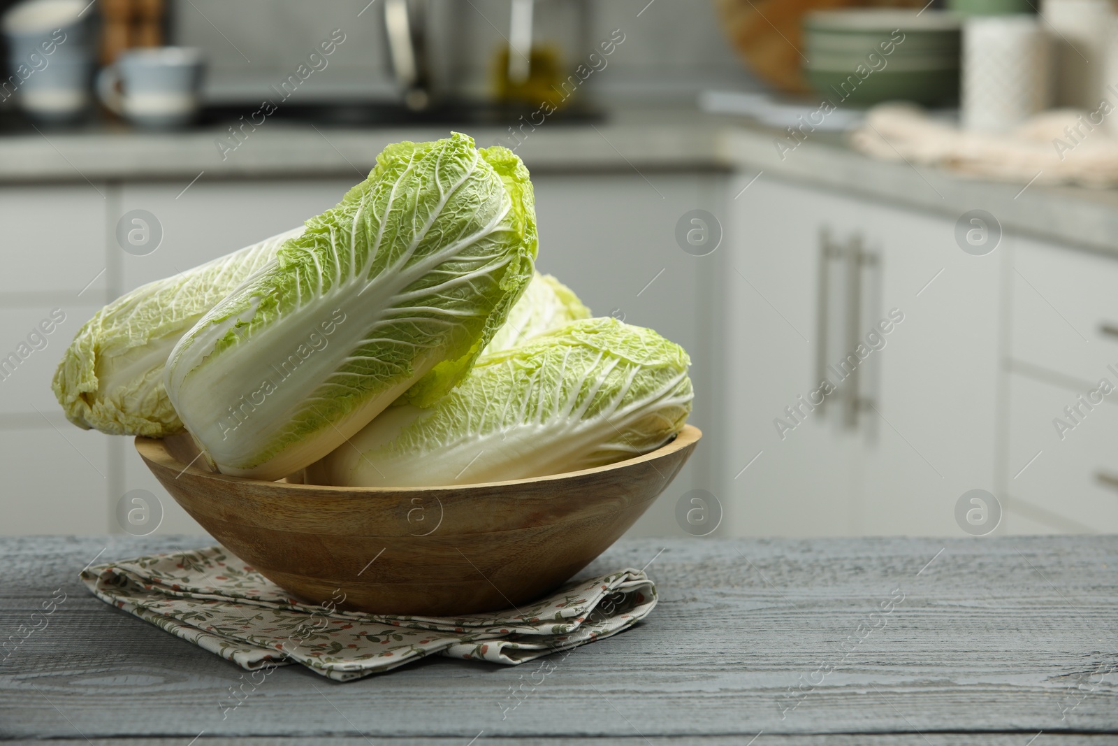 Photo of Fresh Chinese cabbages in bowl on grey wooden table indoors, space for text