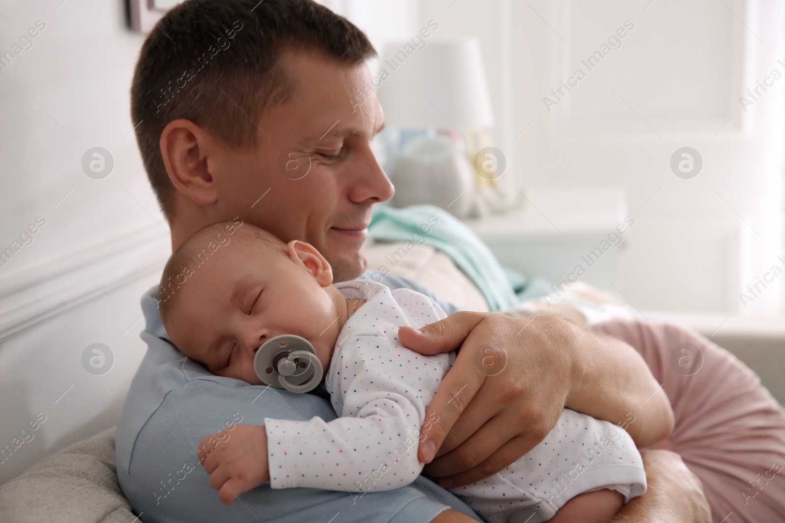 Photo of Happy father holding his cute sleeping baby with pacifier at home