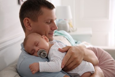 Happy father holding his cute sleeping baby with pacifier at home