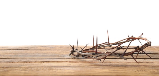 Photo of Crown of thorns on wooden table against white background, space for text. Easter attribute