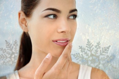 Image of Winter skin care. Woman applying lip balm. Snowflakes on background