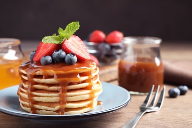 Delicious pancakes with fresh berries and syrup on wooden table