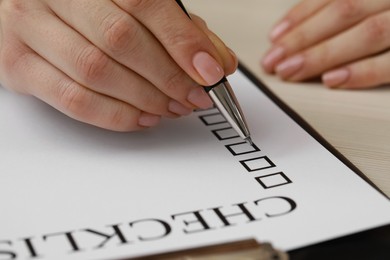 Photo of Woman filling Checklist at white wooden table, closeup