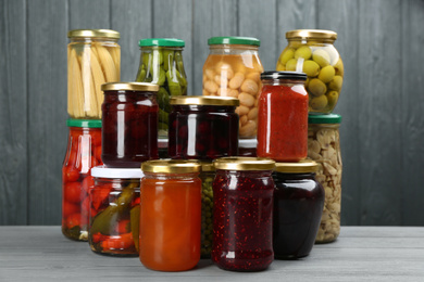 Glass jars with different pickled foods on grey wooden background