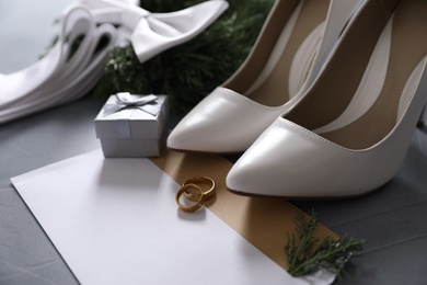 Photo of Composition with wedding rings, white high heel shoes and decor on grey background