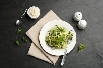 Photo of Delicious zucchini pasta with basil served on black slate table, flat lay
