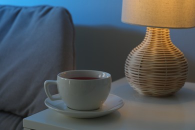 Cup of hot tea and nightlight on white table at night