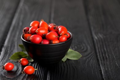 Photo of Ripe rose hip berries with green leaves on black wooden table. Space for text