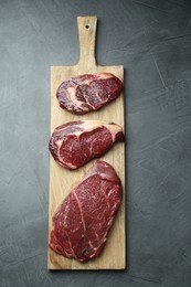 Wooden board with pieces of raw beef meat on grey table, top view