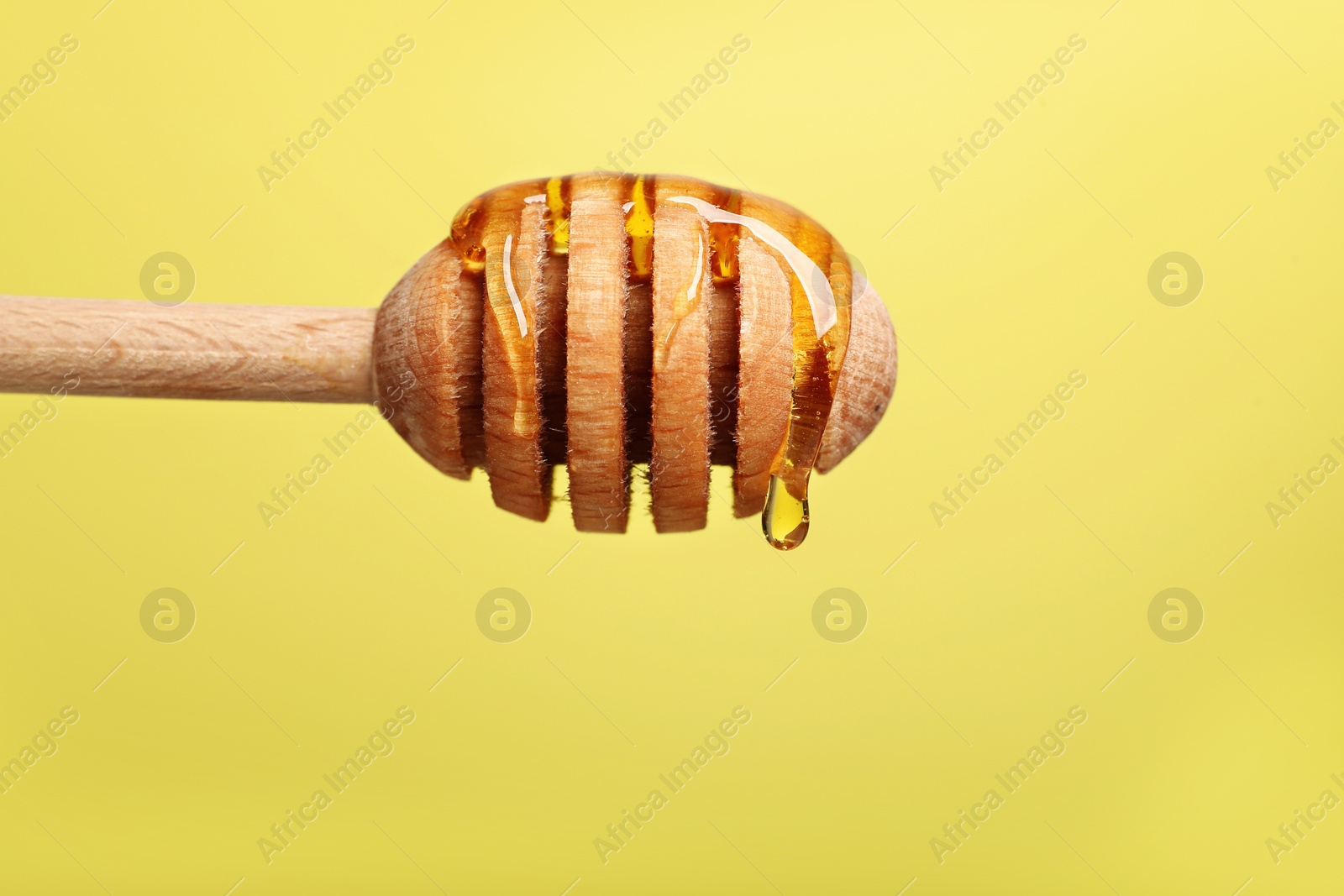 Photo of Delicious honey flowing down from dipper against yellow background, closeup. Space for text