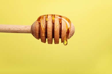 Photo of Delicious honey flowing down from dipper against yellow background, closeup. Space for text