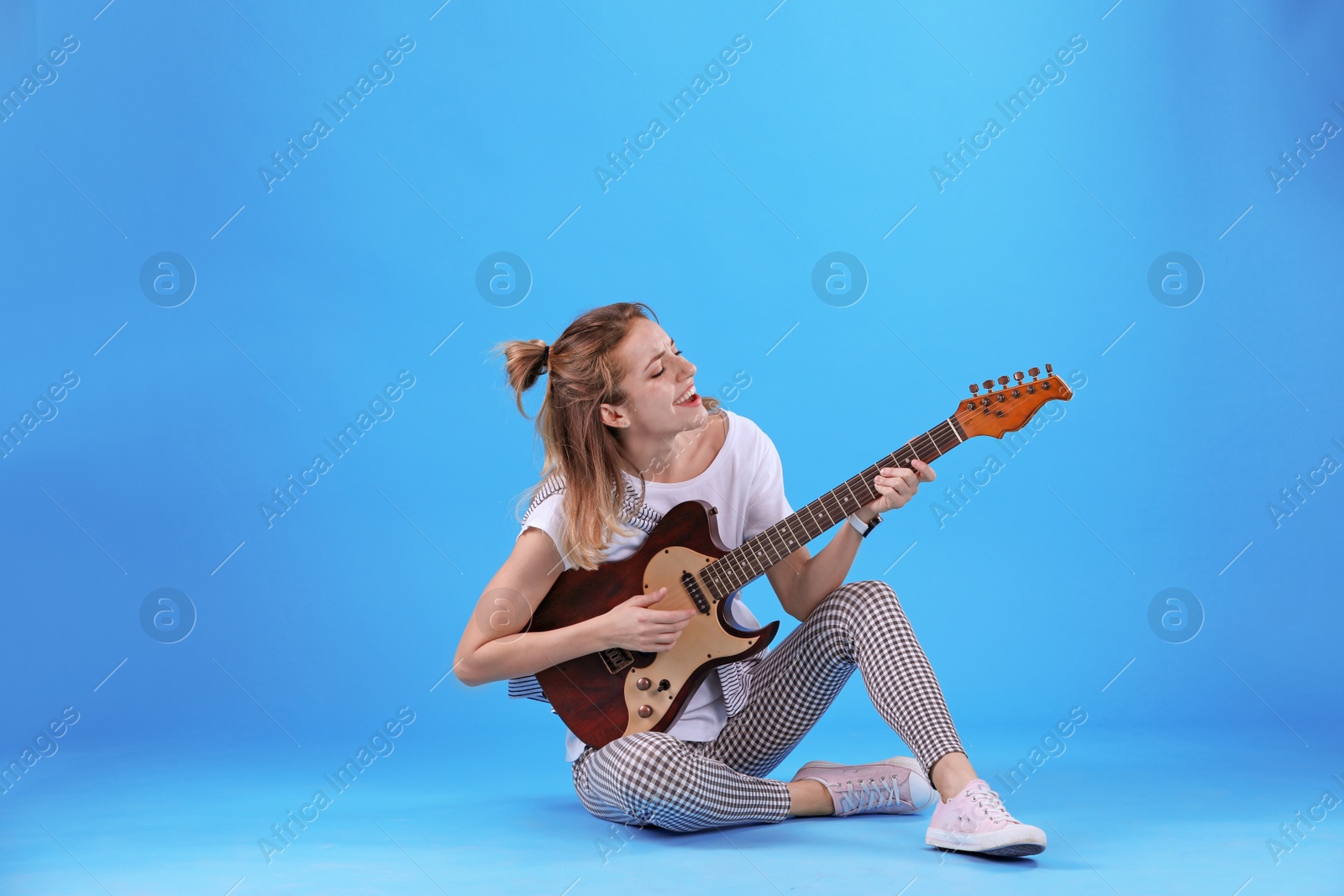 Photo of Young woman playing electric guitar on color background