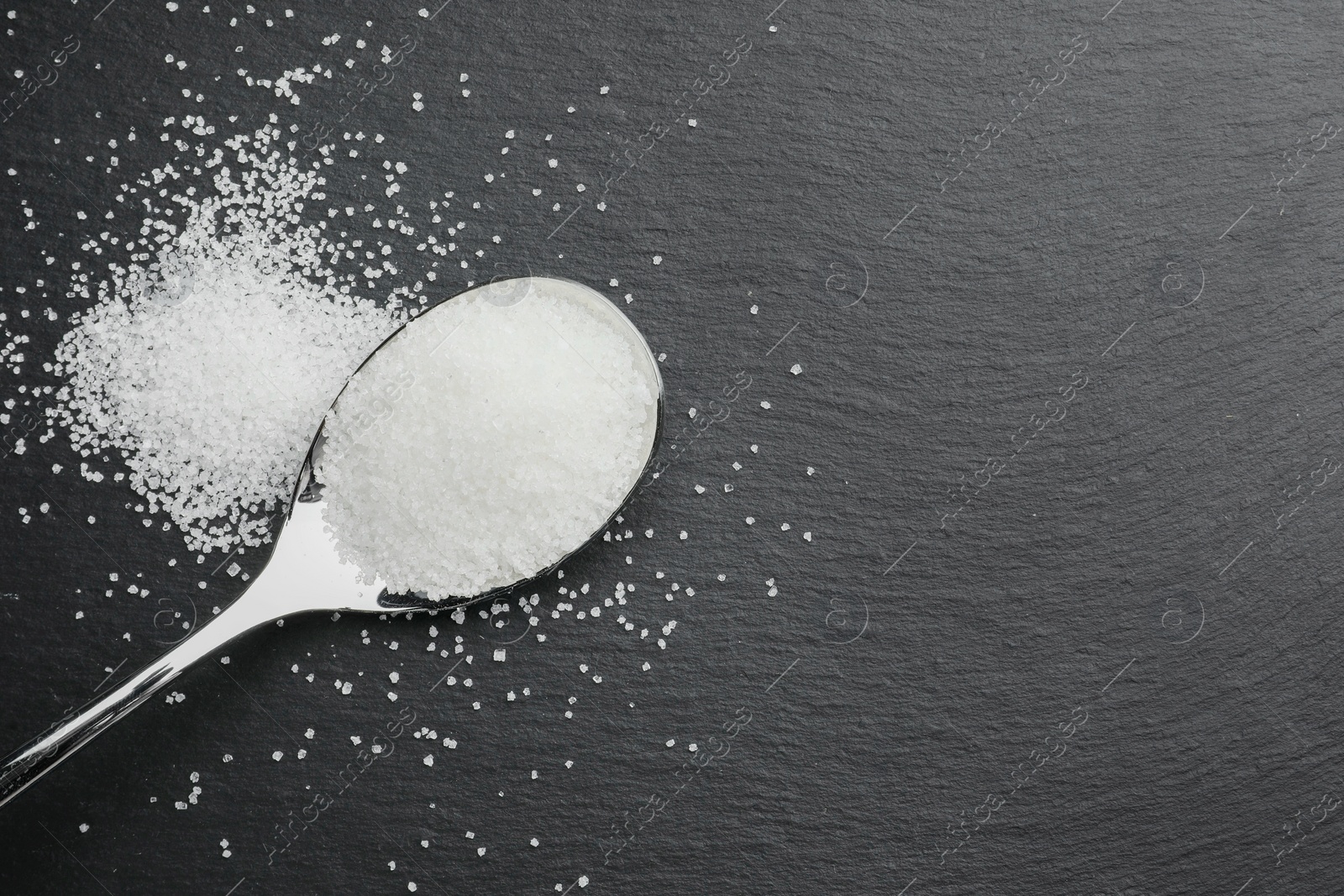 Photo of Granulated sugar and spoon on black table, top view. Space for text