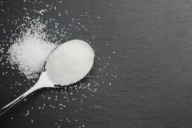 Granulated sugar and spoon on black table, top view. Space for text