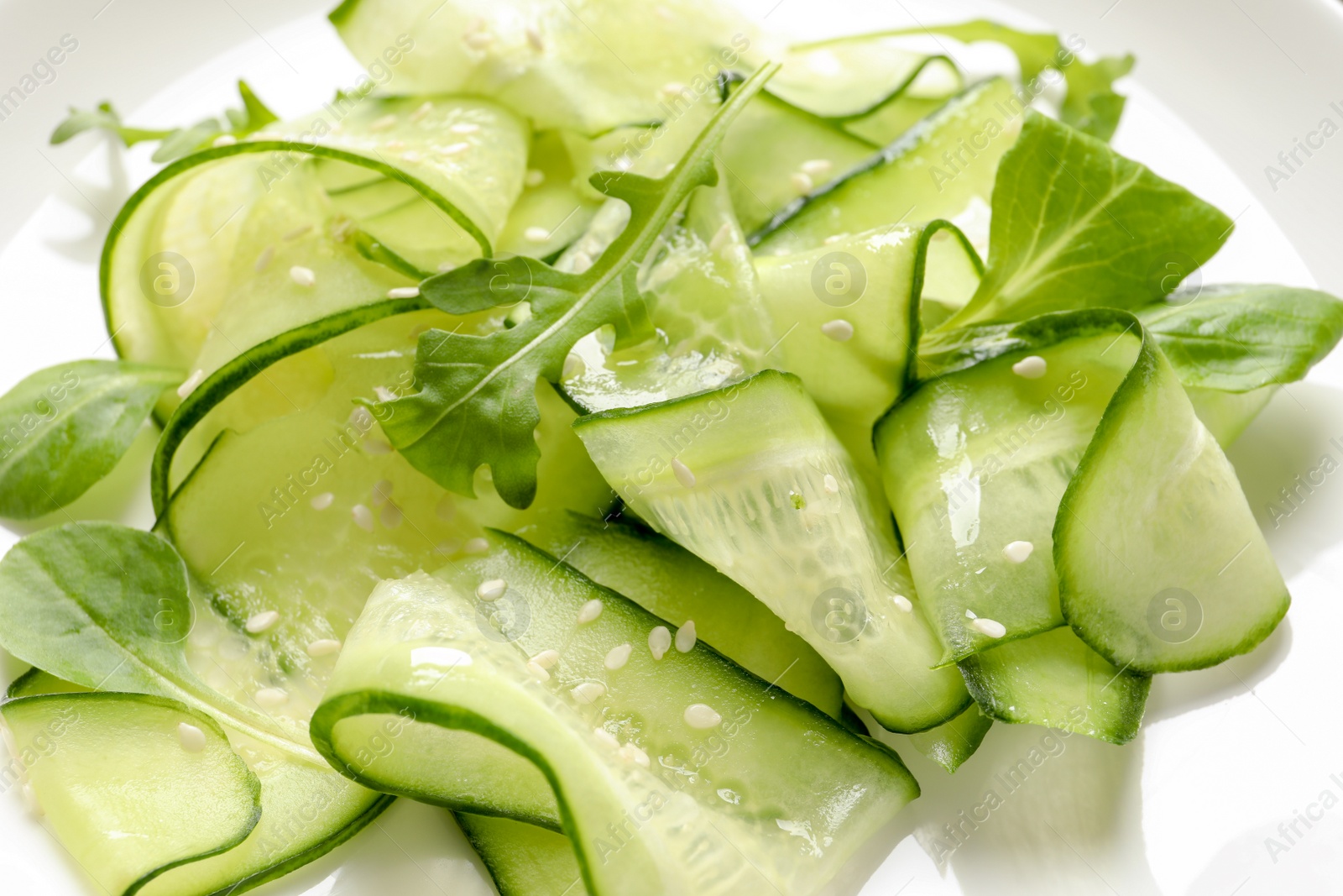 Photo of Delicious cucumber salad with arugula and sesame seeds on plate, closeup