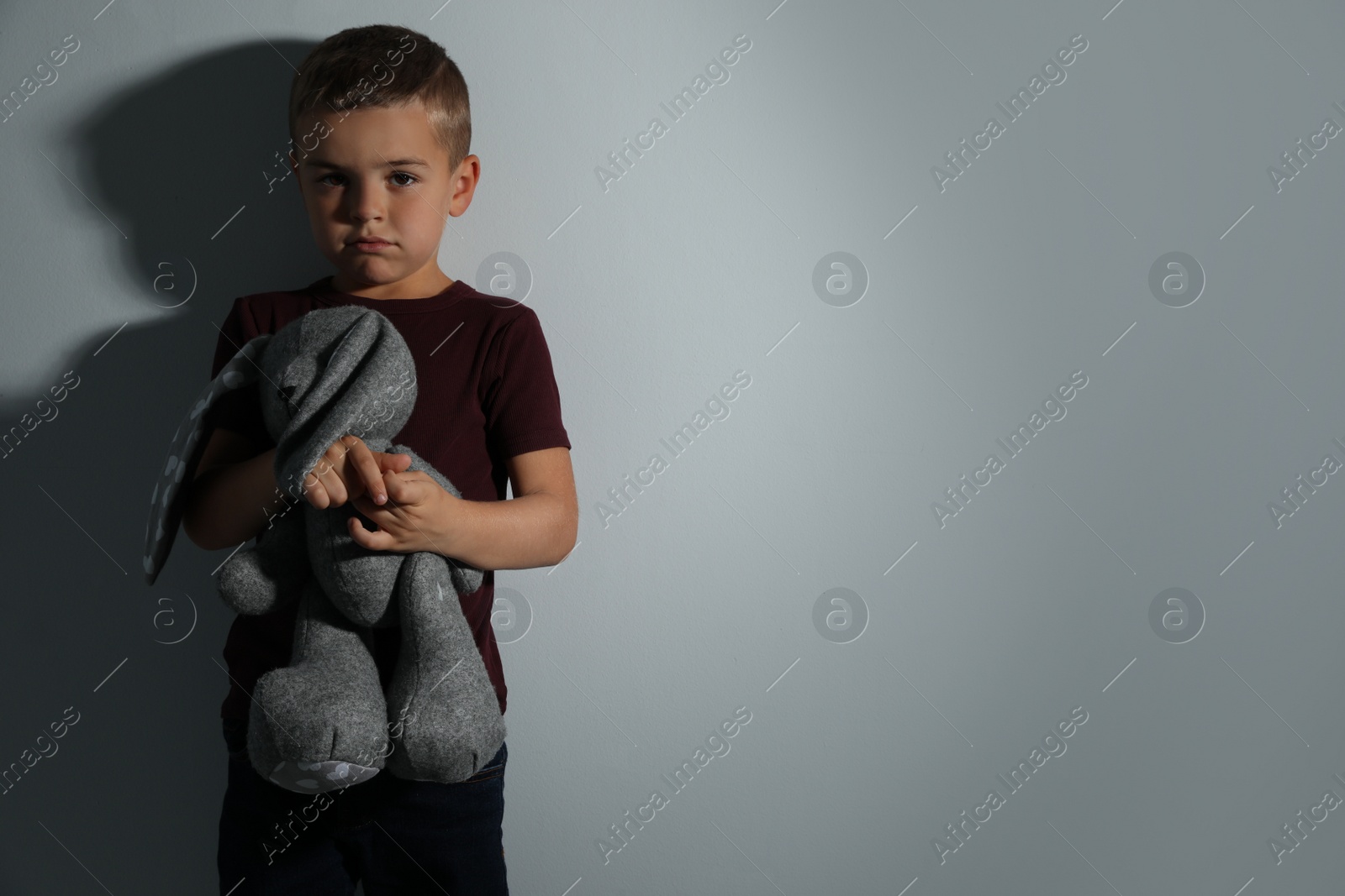 Photo of Sad little boy with toy near white wall, space for text. Domestic violence concept