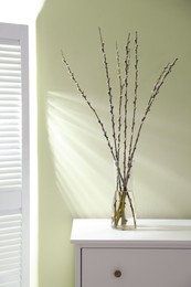 Photo of Glass vase with pussy willow tree branches on white chest of drawers indoors