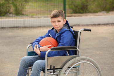 Photo of Upset boy in wheelchair with ball on sports ground