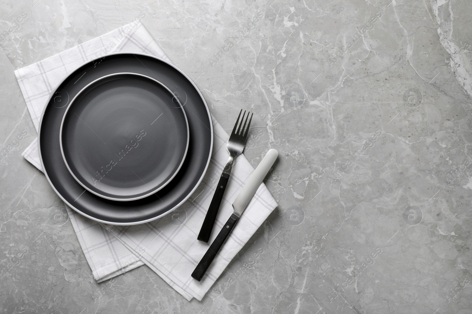 Photo of New dark plates, cutlery and napkin on light grey marble table, flat lay. Space for text