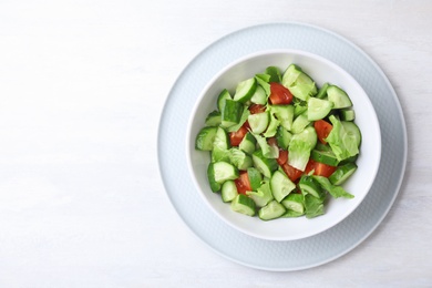 Bowl of vegetarian salad with cucumber, tomato and lettuce on light background, top view. Space for text