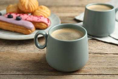 Aromatic coffee in cups, tasty eclairs and profiteroles on wooden table