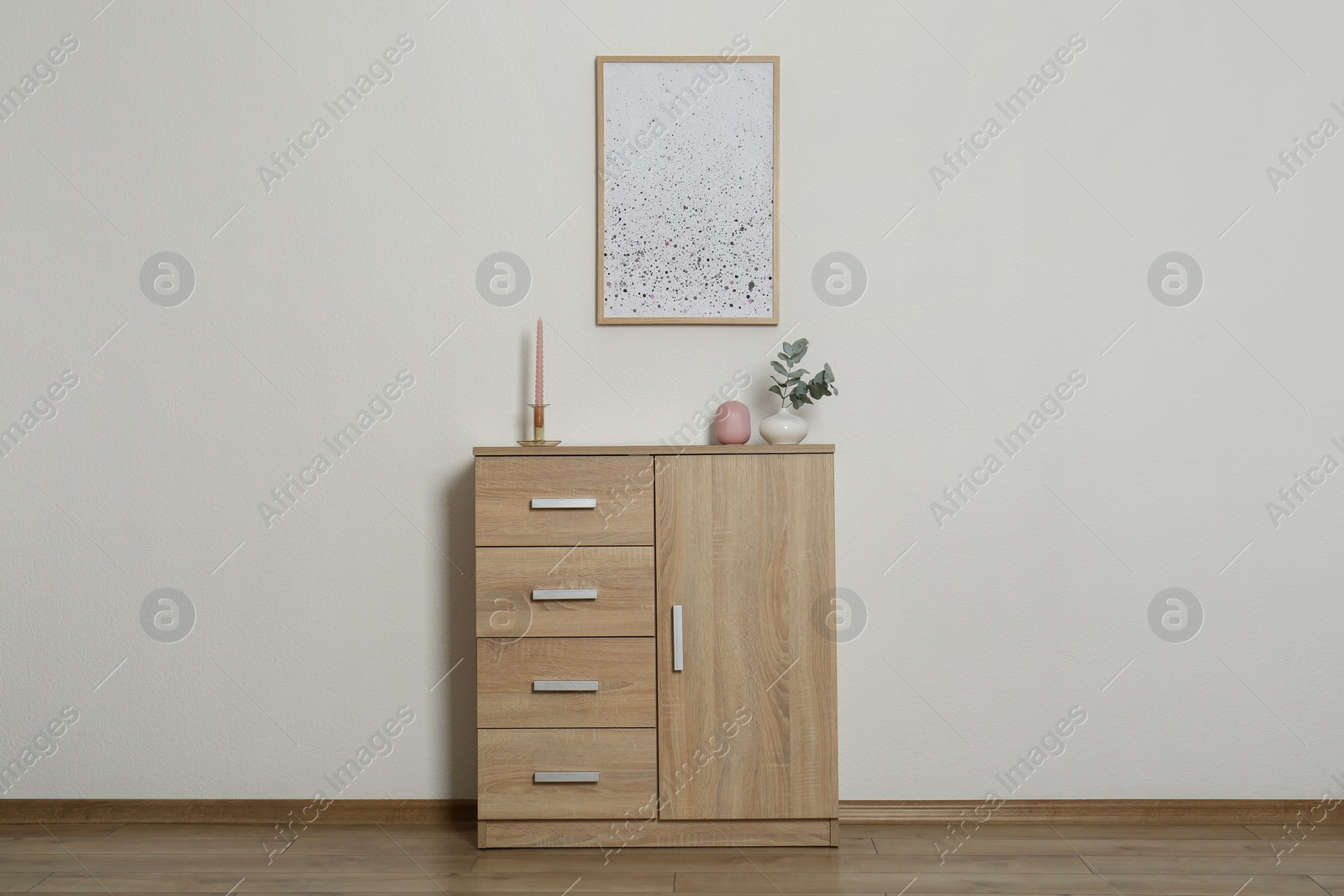 Photo of Chest of drawers, decorative elements and frame in room with light wall. Interior design