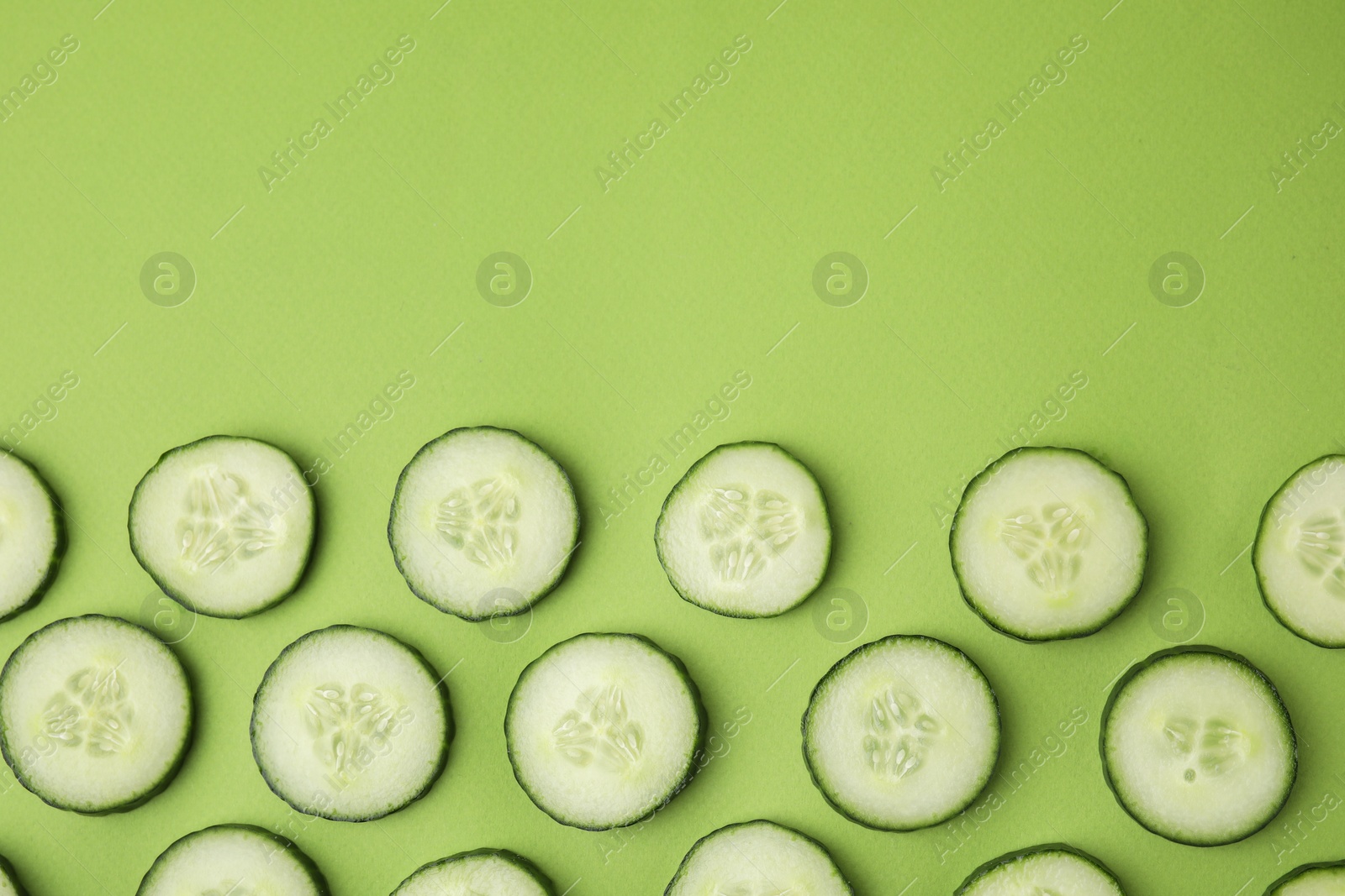 Photo of Fresh slices of cucumbers on green background, top view. Space for text