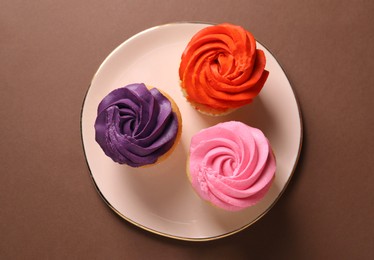 Photo of Delicious cupcakes with bright cream on brown background, top view