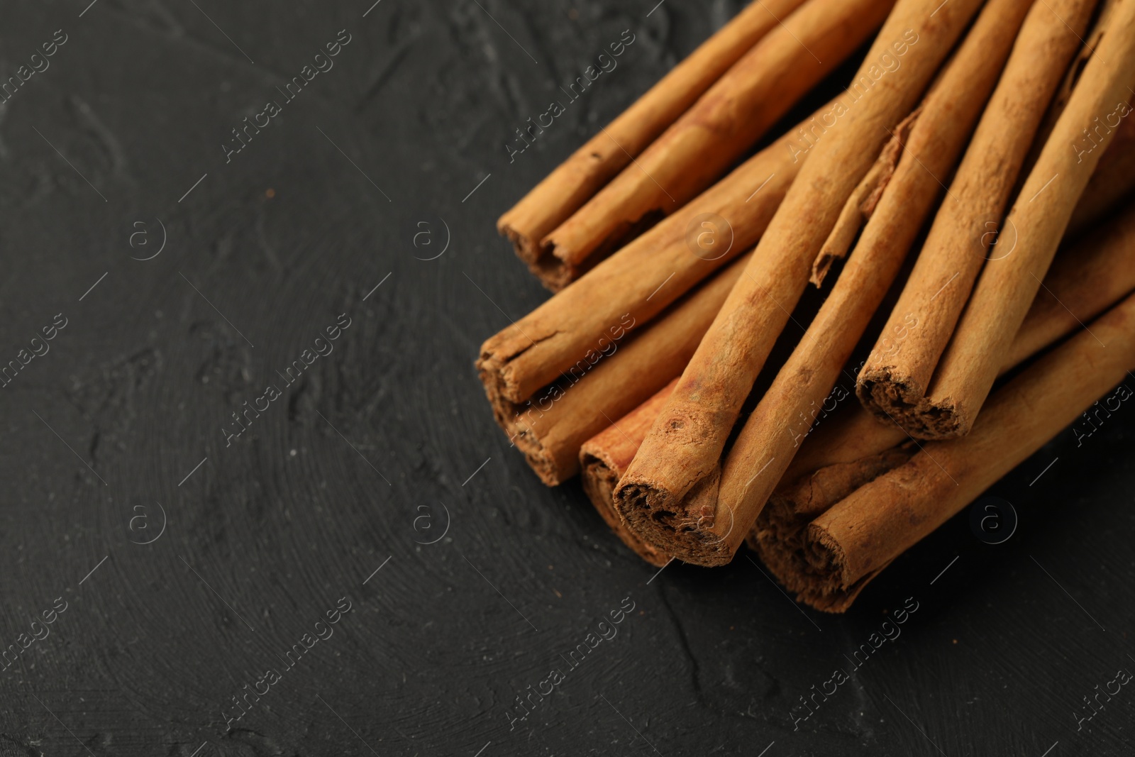 Photo of Dry aromatic cinnamon sticks on black table, closeup. Space for text