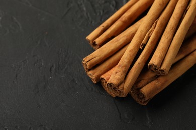 Photo of Dry aromatic cinnamon sticks on black table, closeup. Space for text