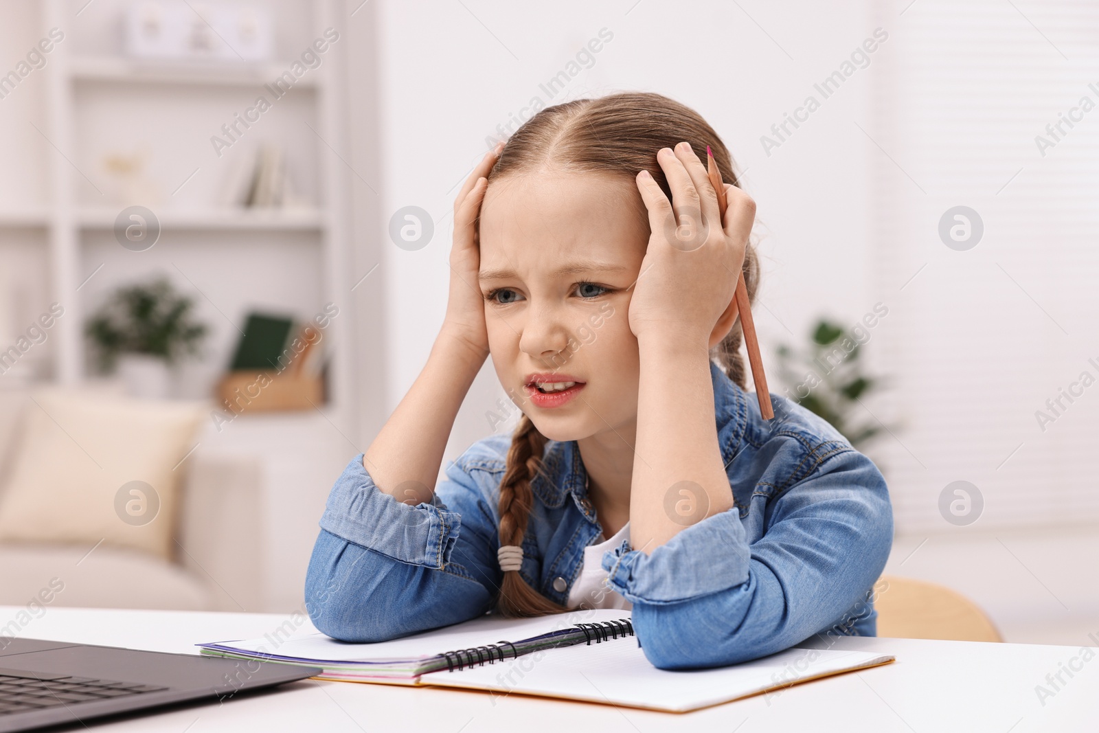 Photo of Little girl suffering from headache while doing homework at home