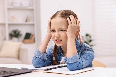 Little girl suffering from headache while doing homework at home