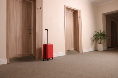 Photo of Modern red suitcase in empty hotel corridor