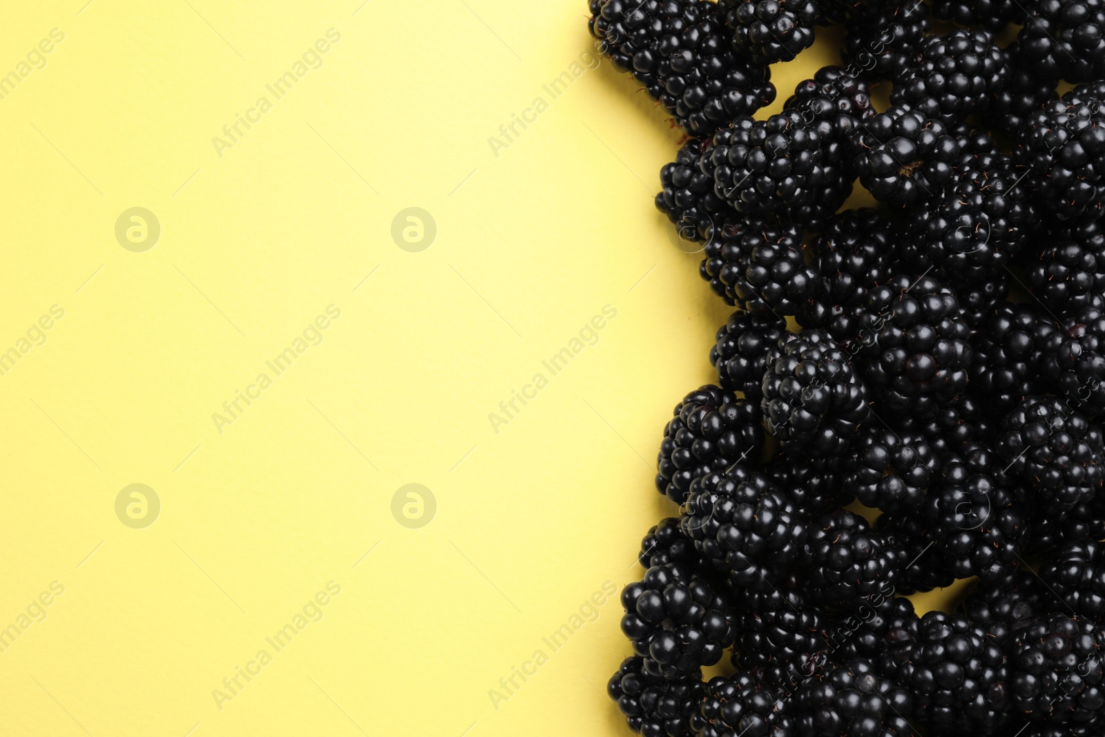 Photo of Tasty ripe blackberries on yellow background, flat lay. Space for text