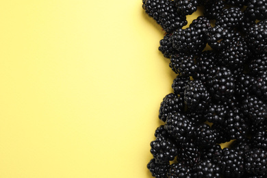 Tasty ripe blackberries on yellow background, flat lay. Space for text