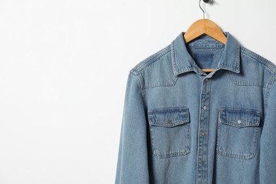 Photo of Hanger with denim shirt on white wall, space for text