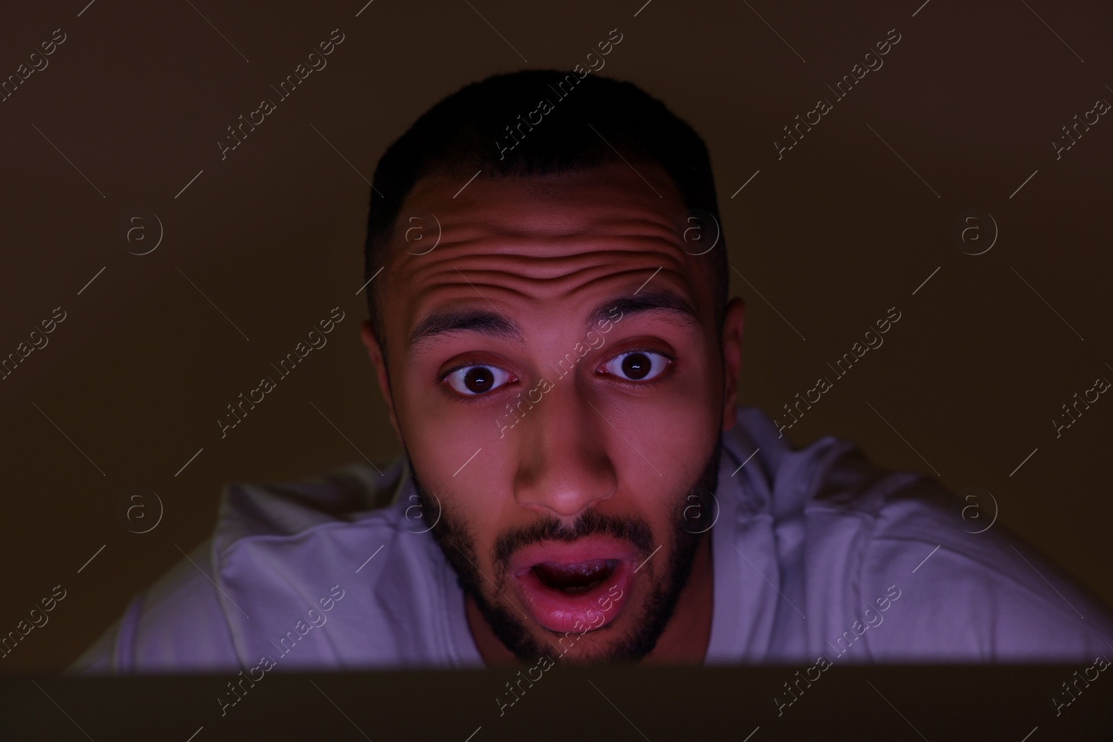 Photo of Shocked man using computer at night. Internet addiction