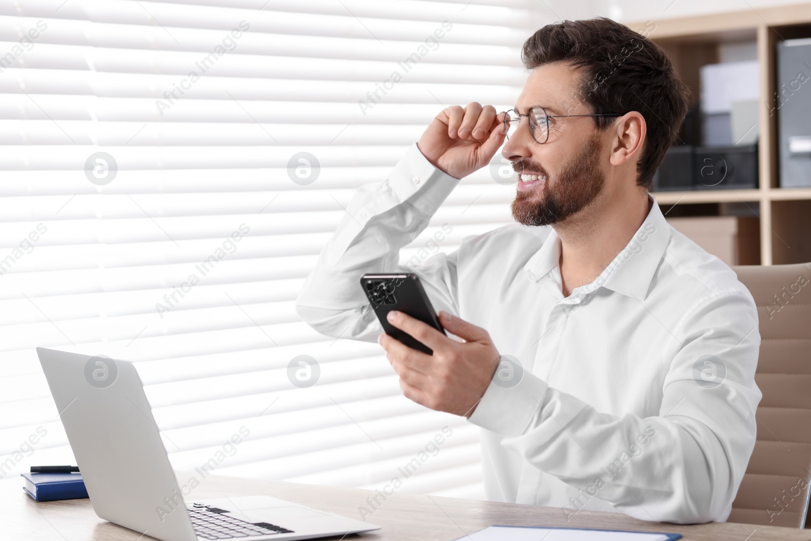 Photo of Smiling man with smartphone at table in office