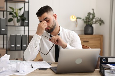 Overwhelmed man sitting at table with laptop and documents in office