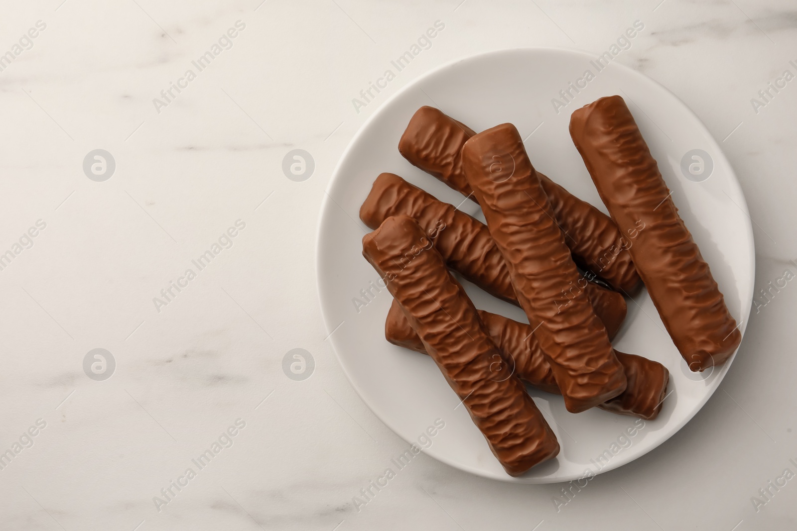 Photo of Sweet tasty chocolate bars on white marble table, top view. Space for text