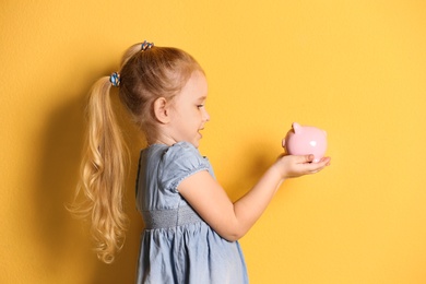 Little girl with piggy bank on color background