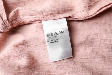 Photo of Clothing label on beautiful pink garment, top view